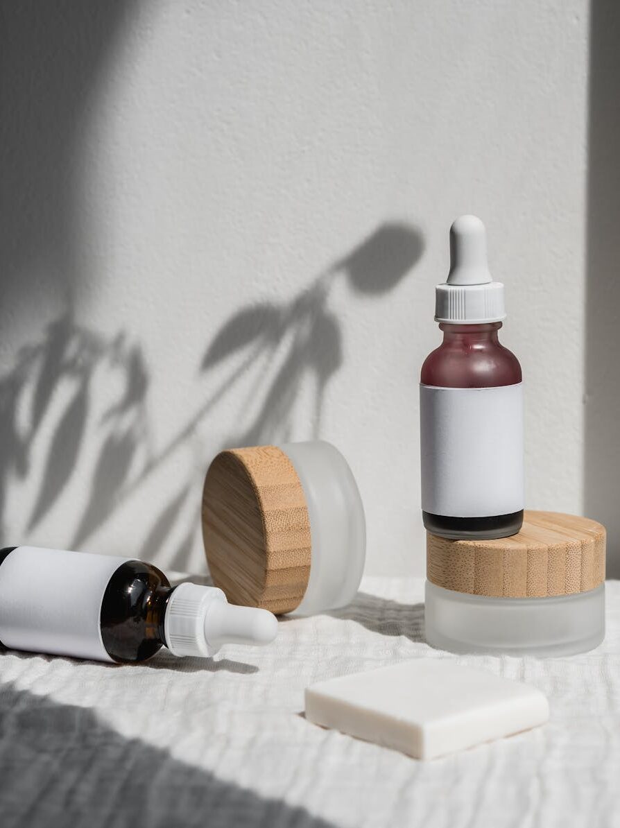 Minimalist arrangement of natural cosmetic jars and droppers with wooden lids, featuring soft shadows and bright lighting.